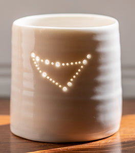 A ceramic porcelain tealight holder, with the Capricorn astrological constellation pierced into it with tiny holes, allowing candlelight to twinkle through. Natural glossy glaze, almost translucent. Horoscope, astrology, zodiac.