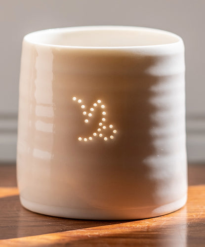 A ceramic porcelain tealight holder, with the Capricorn astrological symbol pierced into it with tiny holes, allowing candlelight to twinkle through. Natural glossy glaze, almost translucent. Horoscope, astrology, zodiac.