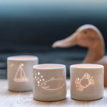 Load image into Gallery viewer, Three porcelain tealight holders, with a crab design, a whale, and a sailing boat. The designs are pierced into it with tiny holes that let the light shine through. These ceramic candle votives are perfect for seaside holidays.
